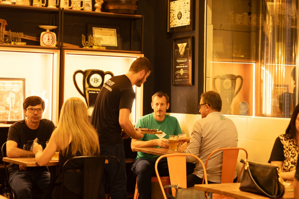 Garçom serve clientes no salão da Big Jack Cervejaria, em um ambiente acolhedor com referências aos prêmios da marca.